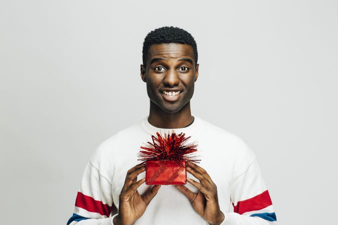 Excited Black man holding up a present wrapped in red with both hands