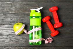 Bottle, measuring tape and apple on wooden background, copy space