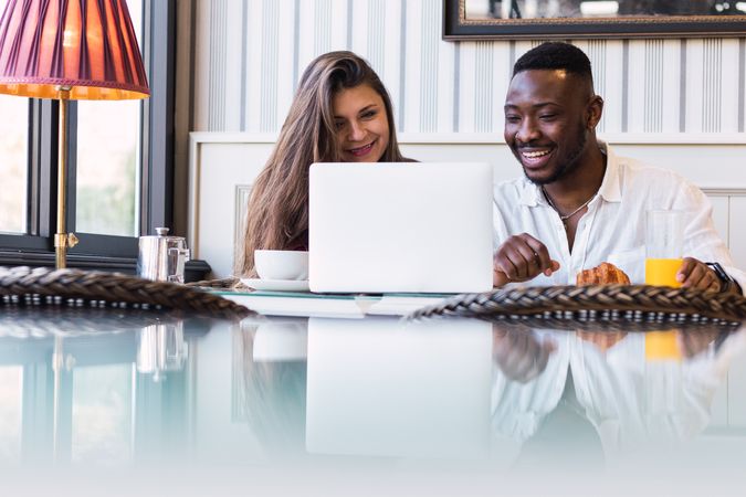 Cheerful multiethnic couple using laptop during breakfast at home