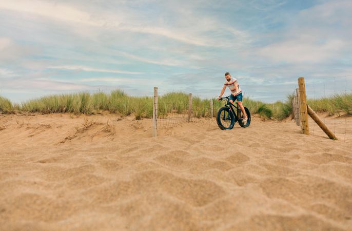 White male riding bicycle along sandy dune