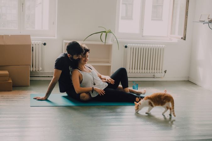 Loving couple cuddling on floor while cat walking around