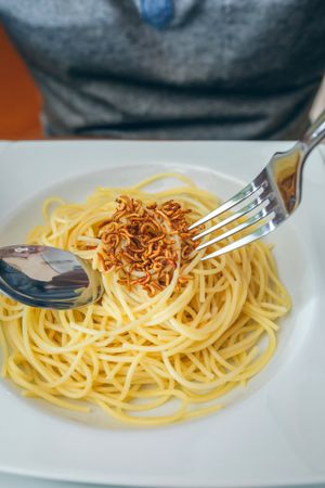Hands of man eating spaghetti with worms