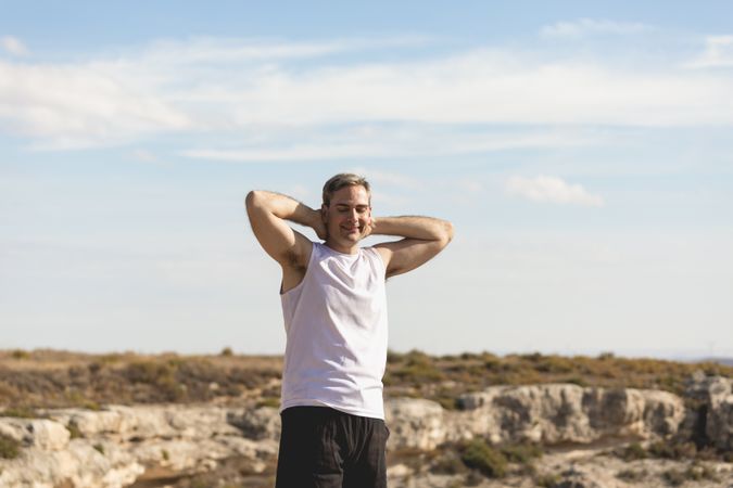 Fit man with hands behind head after working out in rugged terrain
