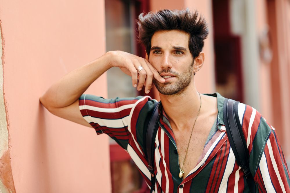 Curious man with dark hair standing outside looking in the distance with hand to his face