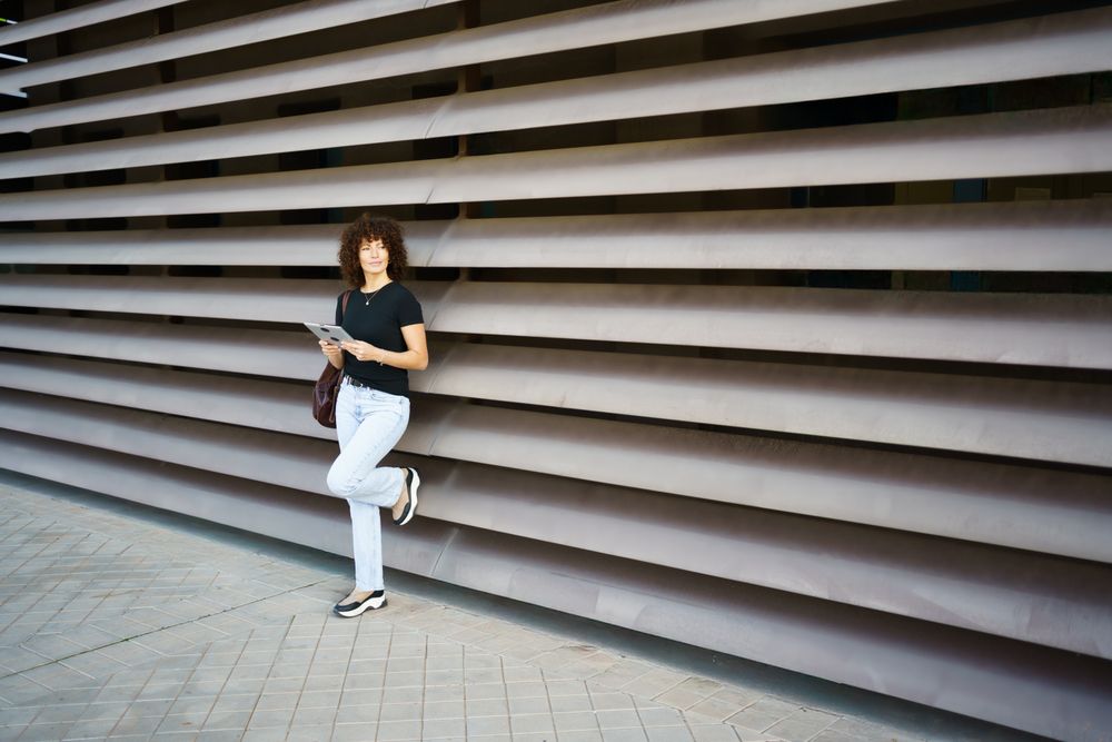 A casual young woman is leaning against a modern architectural wall, radiating confidence and style