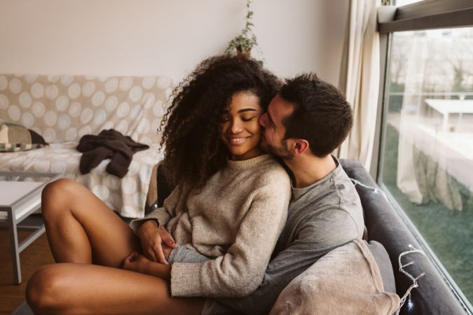 Young multiracial couple hugging on sofa