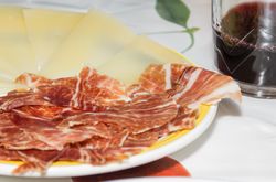 Typical spanish tapa with slices of serrano ham and manchego cheese, accompanied with a glass of Rioja red wine