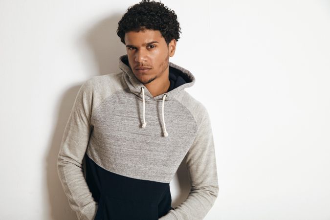 Man in grey sweater with serious expression leaning on wall