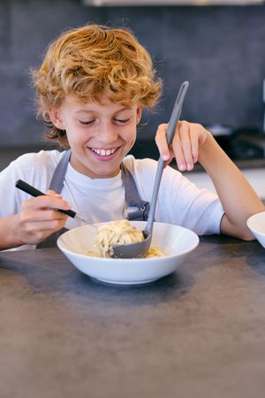 Content boy enjoying tasty spaghetti at table in house