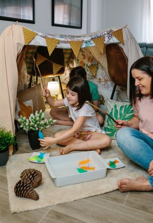Happy mother and daughter camping at home playing diy fishing game