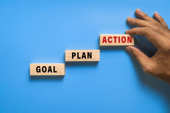 male hand put goal, plan, action words text on wooden blocks isolated on blue background