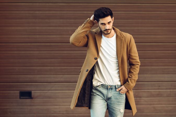 Man in smart winter jacket in front of brown wall touching hair