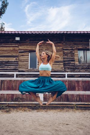 Flexible woman in colorful skirt dancing at rural paddock