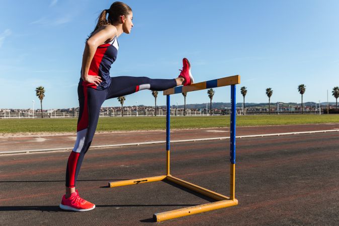 Female athlete stretching on hurdle on stadium