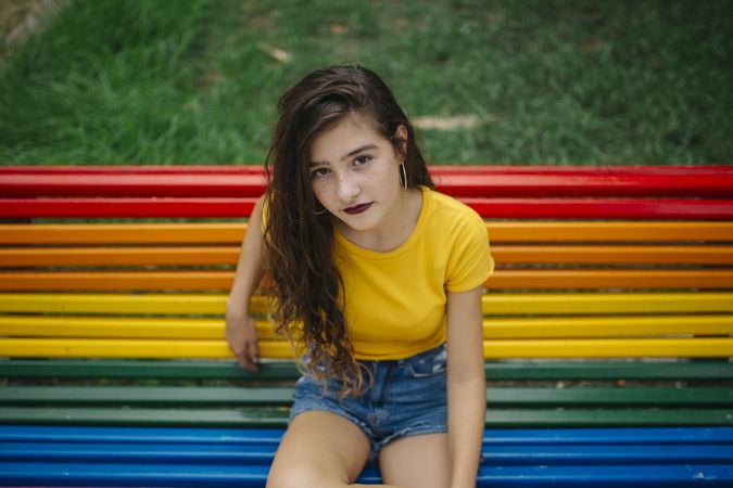 Cheerful woman sitting on rainbow bench
