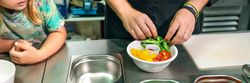 Unrecognizable chef preparing vegan poke bowl while little girl watching him in professional kitchen