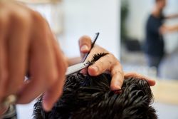 Crop hairstylist cutting hair of client