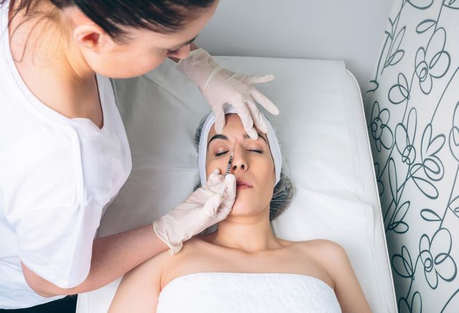 Aesthetician injecting botox between female's eye in a beauty salon