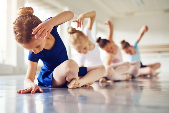 Girls sitting in ballet class doing a stretch on the floor
