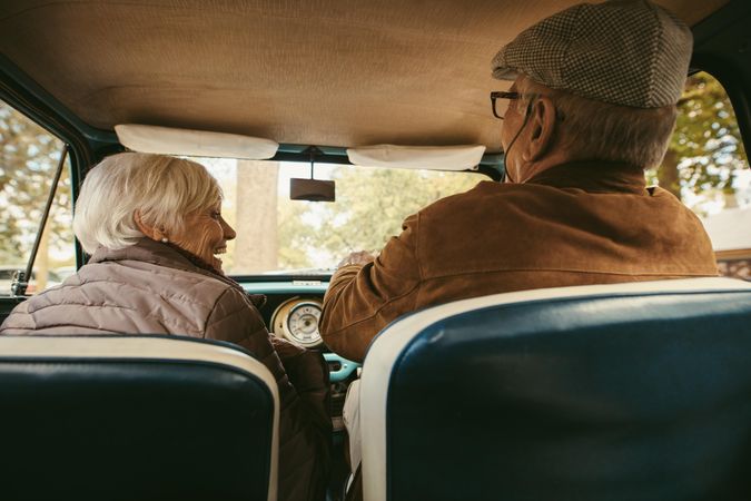 Older man wearing hat driving the car and talking to a woman sitting on passenger seat