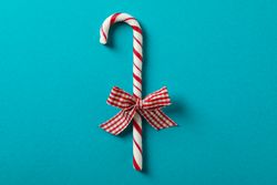 Sweet candy cane with bow on turquoise background, space for text
