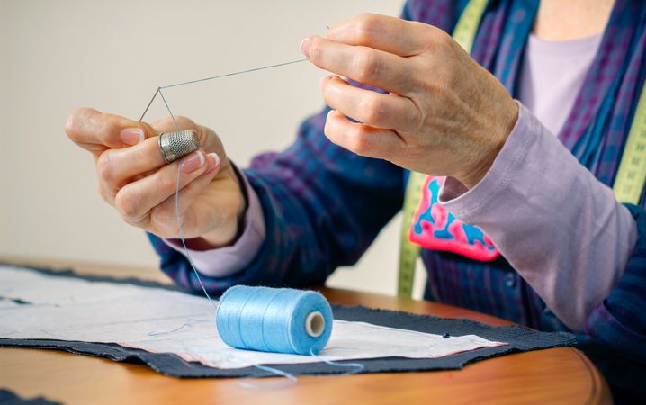 Mature female dressmaker threading a needle