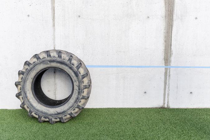Heavy tire on grass near grey wall