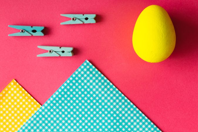 Yellow Easter egg on pink paper with clothes pins