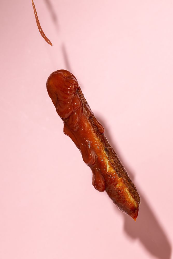 delicious grilled sausage full of ketchup in a pink background