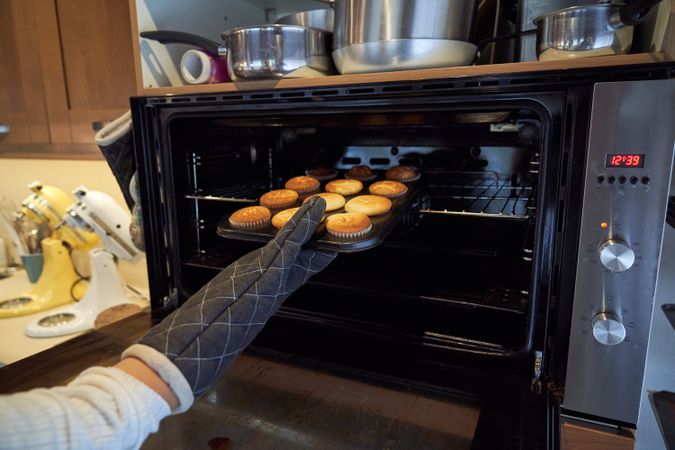 Unrecognizable person taking cupcakes from oven