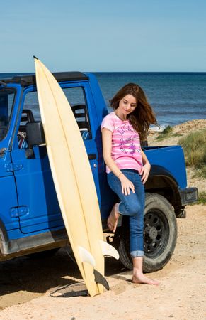 Woman with surfboard near car at seaside