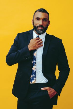 Confident Black male in suit with floral tie in yellow studio