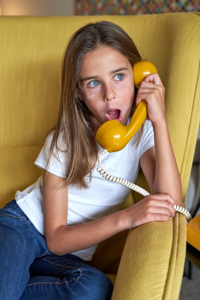 Astonished girl talking on retro telephone in room
