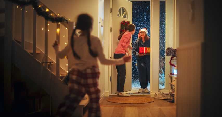 Young Mother Meeting Grandparent by the Door in a Decorated Home with Garlands, Small Boy and Girl Running to Meet Their Grandmother with Christmas Gifts and Presents