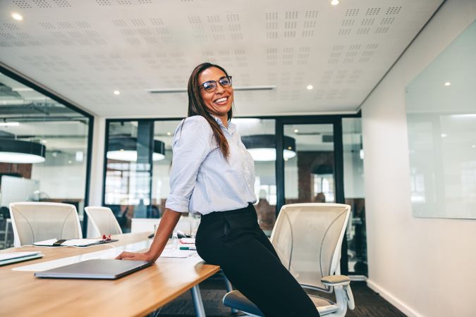 Businesswoman smiling cheerfully in a boardroom leaning on modern desk