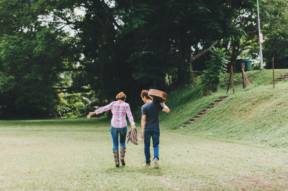 Back view of man with guitar and woman walking on green grass field