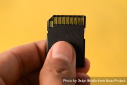 Close up of SD card in hand with yellow background and space for text 5ngWL8