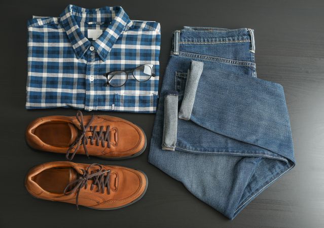 Flat lay composition with jeans, shirt, glasses and shoes on table