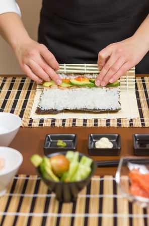 Hands of woman chef arranging filling in rice to roll sushi in a nori seaweed sheet, vertical