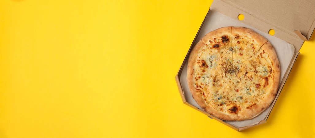 Cheese pizza in carton box on yellow background