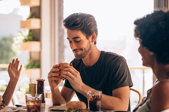 Man hanging out at cafe with friends and eating burger