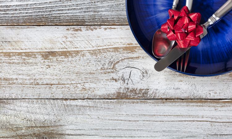 Partial holiday dinner table setting with cutlery and dark blue plate on rustic wood table