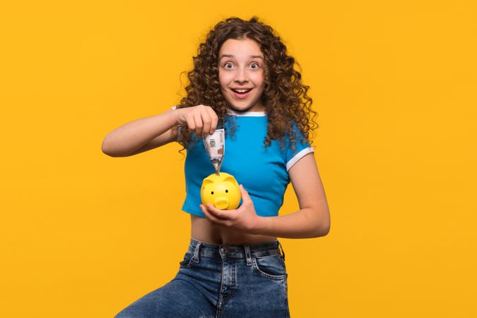 Surprised girl putting money into a piggy bank
