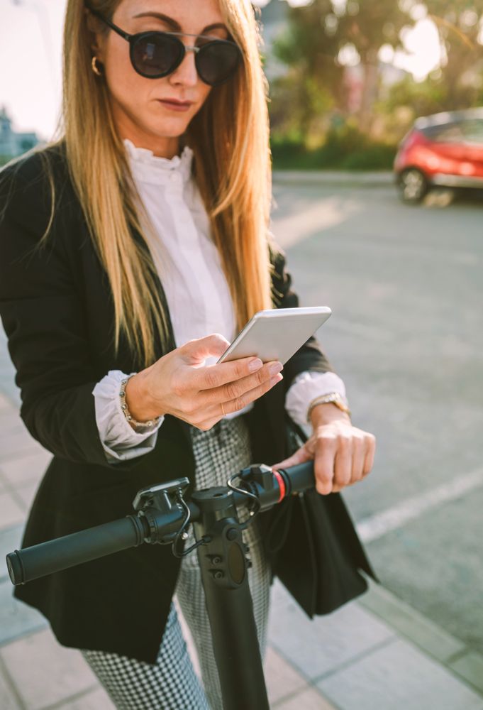 Businesswoman with e-scooter looking at cellphone
