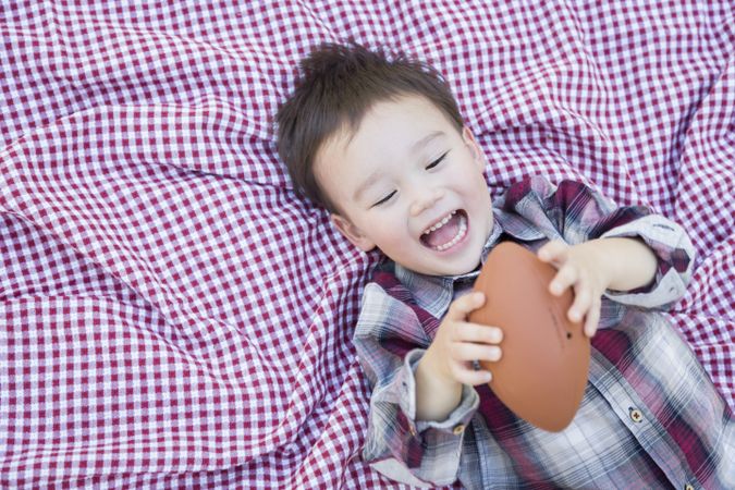 Toddler Boy Playing with Football on Picnic Blanket