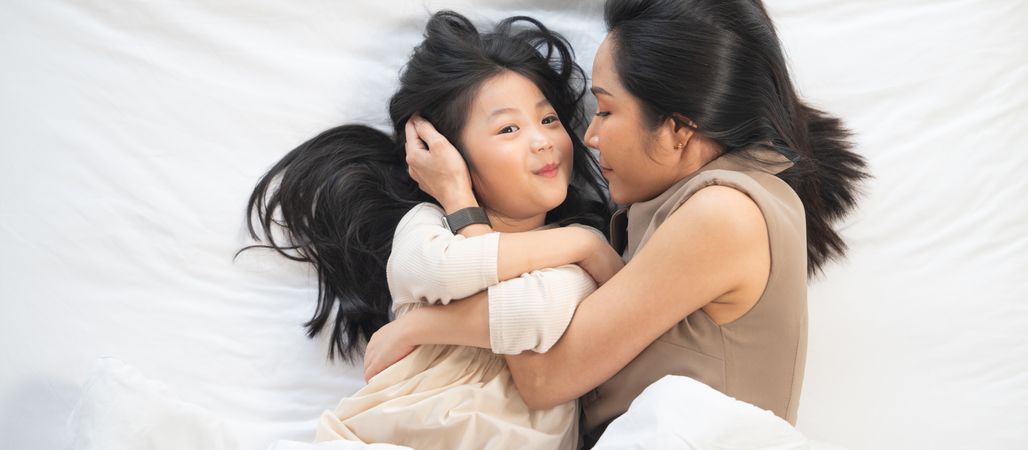 Top view of Asian mother and daughter cuddle and talking on bed.
