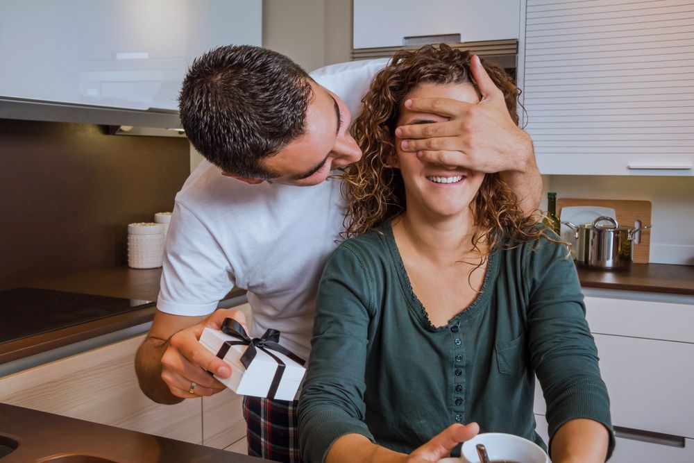 Husband surprising wife with giftbox in kitchen