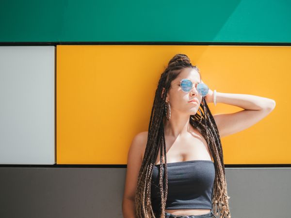 Charming teenage girl with dreadlocks in sunglasses nearby colorful wall