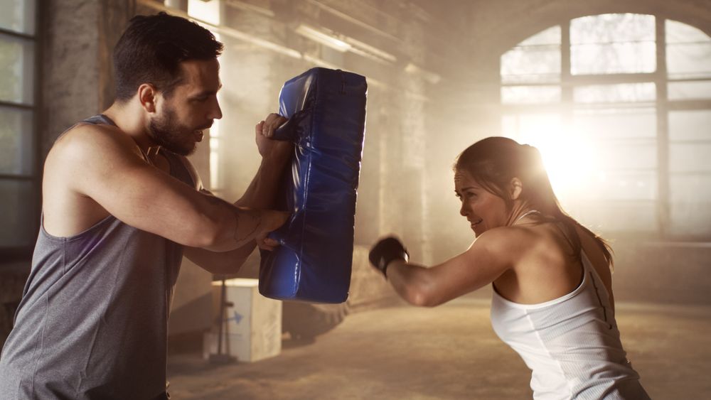 Athletic Woman Trains Her Punches on a Punching Bag that Her Partner  Trainer Holds.