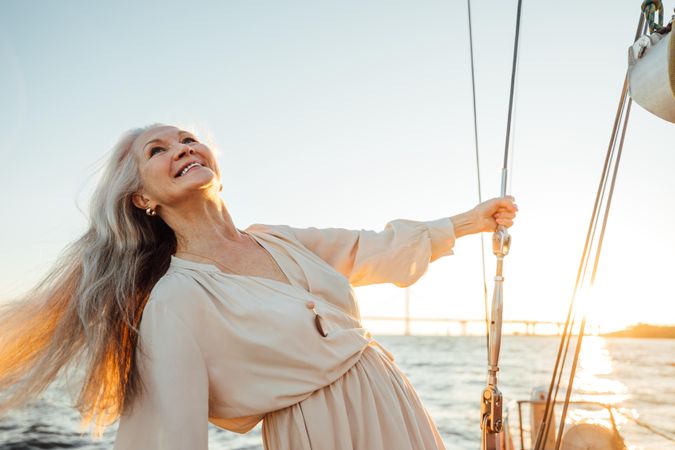 Mature woman with gray hair enjoying a sailboat at sunset